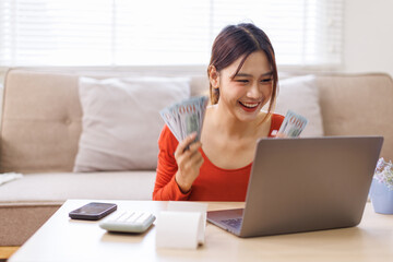 Money cash dollar rain falling, Financial concept. Make money on the Internet. Asian woman sitting on the desk and working with a laptop celebrating success play casino online game.

