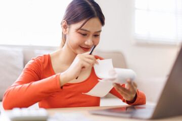 Happy asian woman manage household budget calculate expenses expenditures on machine. Smiling young...