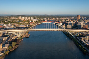 Fototapeta premium Aerial drone picture of Portland’s Fremont Bridge at sunset, the Willamette River, Downtown Portland, industrial area, and Mt. Hood in the background, with clear blue summer sky