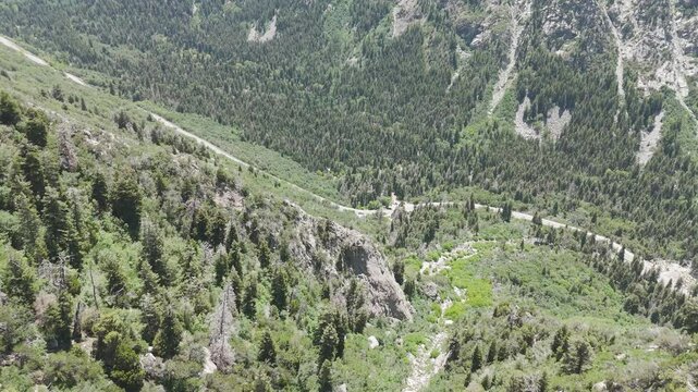 Aerial - Flying down mountain slope toward winding road in the bottom of the canyon with traffic on the road
