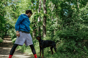 Man training doberman pinscher guard dog in forest path