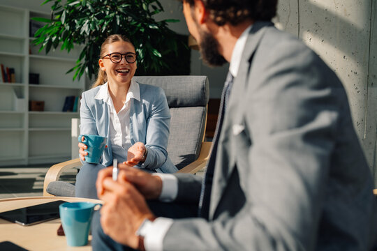 Businesswoman holding coffee mug talking to businessman in office lounge area