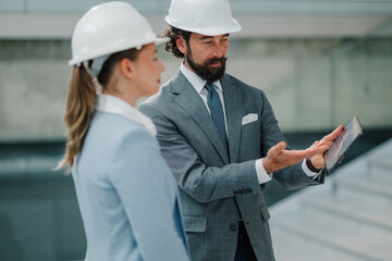 Architects wearing hardhats using tablet and discussing project inside modern building