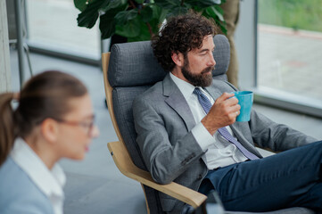 Businessman relaxing on modern chair drinking coffee in office