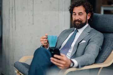 Businessman relaxing with coffee and smartphone in modern office
