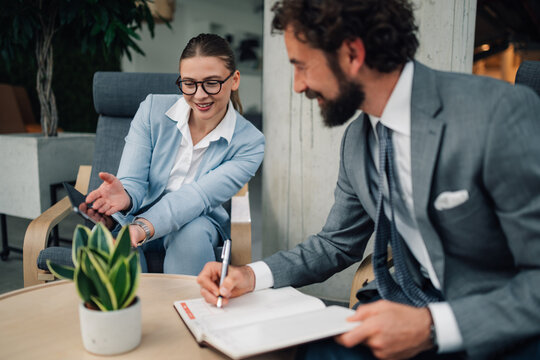 Businesswoman showing tablet to businessman taking notes in modern office