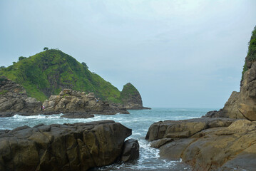 Rugged coastal landscape at Pantai Payangan in Jember features a rocky foreground leading to a calm...