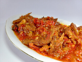 Oval-shaped dish filled with Dendeng, an Indonesian dish featuring thinly sliced, fried beef in a vibrant red chili sauce. Related to spicy dishes, traditional meat preparations, authentic local food
