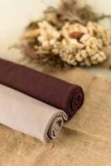 Two Rolled Pashmina Hijabs In Beige And Brown With Dried Flower Decoration On A Burlap Fabric For...