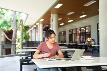 Focused asian teen girl student writing notes in notebook distance learning studying online makes...
