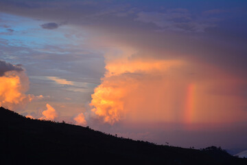 A dramatic sunset sky over a dark landscape, featuring a large, illuminated cloud formation and a...