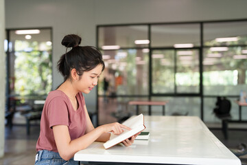 Female student sitting in cafeteria, reading book, studying for final exam at university.