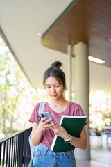 Fototapeta premium Online learning, e-education concept. Happy young asian lady student using phone outdoors, carrying backpack and textbooks, going to university, checking her schedule online.