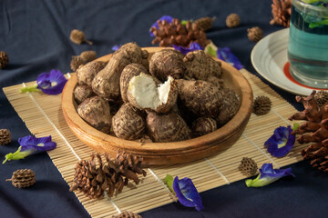 Traditional Asian food ingredient, steamed tora roots served in woodenware, surrounded by butterfly pea flowers and pine cones. 