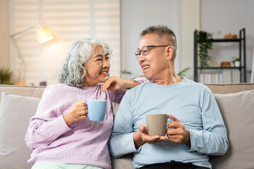Smiling senior couple sitting comfortably together on sofa drinking cup of  coffee, two serene...