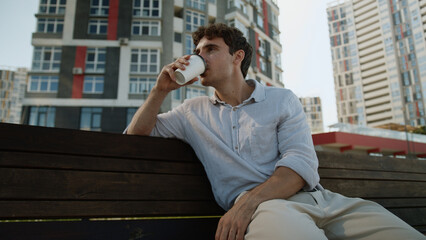 Caucasian European man sitting on bench male holding cup coffee break drinking takeaway order...