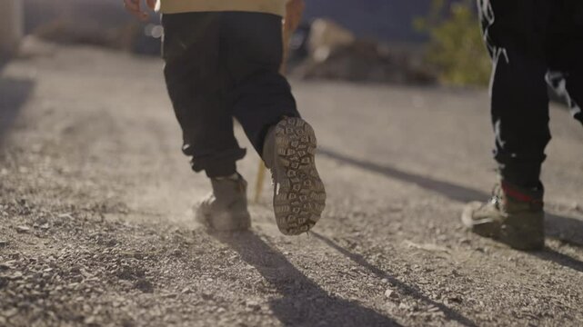 Slow motion close-up of a child&rsquo;s hiking boots walking on dusty ground during a trekking adventure in the High Atlas mountains of Morocco, capturing each step with precision