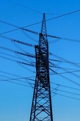 A tall transmission tower stands against a bright blue sky. The power lines connect the tower to...