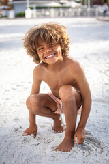 Cute diverse little boy playing in the sand at the beach while on vacation. Digging in the sand with a shovel and bucket