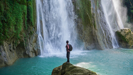 Adventurer standing before powerful waterfall with lush jungle and turquoise water, symbolizing...
