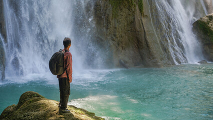 Stunning jungle waterfall with hiker standing on rock near turquoise water, perfect for adventure...