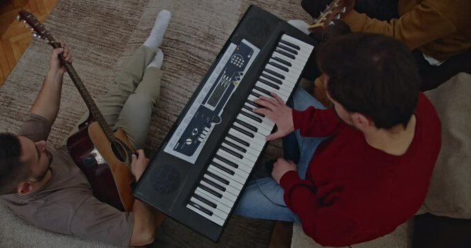 Three friends enjoy their time together, playing music. Two acoustic guitars and a keyboard create a cozy home atmosphere.