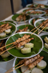 Close-up of Indonesian chicken satay served with sliced rice cake (lontong) on a banana leaf-lined plate, a classic street food and festive dish in Indonesia.