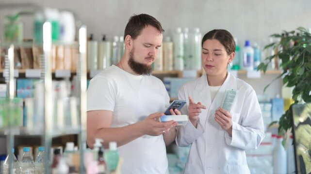  Young man buyer scanning qr code for box of ointment with young woman pharmacist in pharmacy