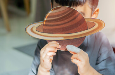 Cheerful little boy with paper model planet in livingroom while playing solar system.