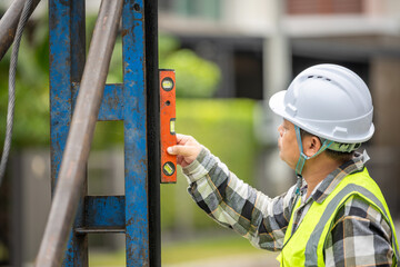 Construction worker in safety helmet and reflective vest using level tool to check horizontal...