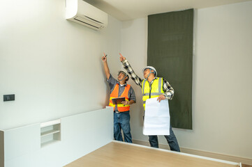 Two construction workers wea safety vests and helmets discussing and inspecting a wall in an indoor...