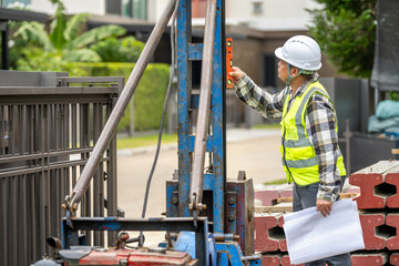 Construction worker wea safety helmet and vest measu building structure with level at outdoor site du project development