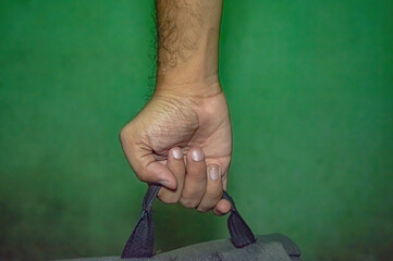 Close up of a hand gripping a backpack strap against a green background, capturing texture,...