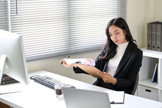 Confident Asian office worker reviewing charts and graphs at her desk in a modern office