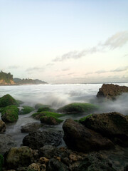 Long exposure of waves crashing on the mossy rocks at a hidden beach in East Java, Indonesia. 