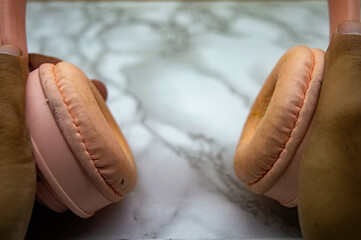 Close up of hands holding worn pink headphones with visible dirt and wear on the ear pads, placed on a marble surface. Ideal for lifestyle, tech usage, and cleaning themes