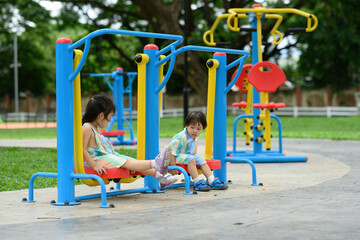 A little boy and a little girl in matching pastel outfits enjoy time on a vibrant playground exercise machine