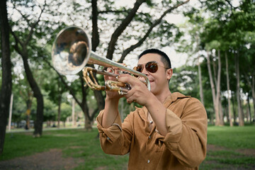 Trumpet player enjoying music under the trees on a sunny day in the park