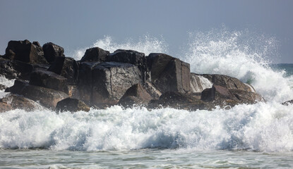 A large rock wall is crashing into the ocean, creating a powerful wave
