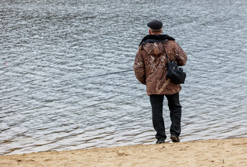 Obraz premium A man is fishing in a lake wearing a brown jacket and black pants