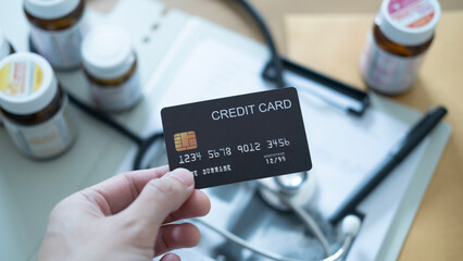 Hand holding a black credit card over medical documents and stethoscope, payment concept.