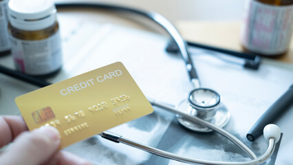 A hand holding a gold credit card near medical documents and stethoscope, payment option.