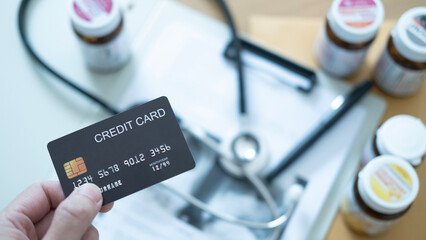 Hand holding a black credit card above medical bills and medicine bottles, symbolizing healthcare payments and financial pressure.