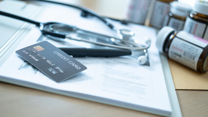 Close-up of a gray credit card on top of patient medical records with pills and stethoscope nearby.