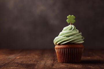 A single cupcake with pale green frosting and a shamrock sits on a dark wooden surface against a blurred background