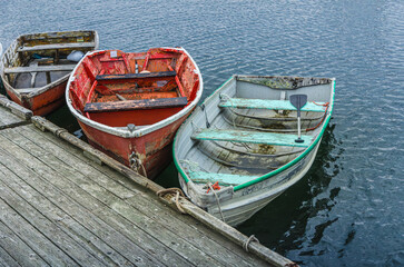 Three weathered small rowboats at a wooden dock in Rockport, Massachusetts, USA