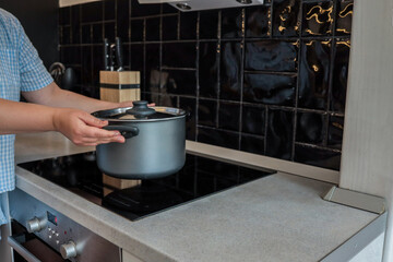 Person placing a pot on a modern induction cooktop in a stylish kitchen with black tile backsplash....