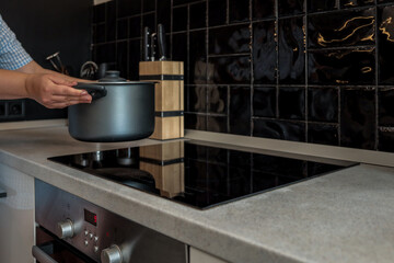 Person placing a pot on a modern induction cooktop in a stylish kitchen with black tile backsplash....