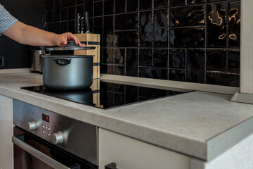 Person lifting the lid of a black pot on a hot induction stove in a modern kitchen. Oven is turned...