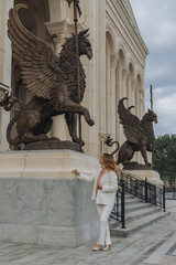 Griffins Statues Building Woman - A woman in a white suit poses next to two griffin statues in...